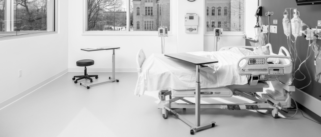 A monochrome photograph of a modern, empty hospital room with a bed, various medical equipment, 还有一扇可以俯瞰外面建筑的大窗户.